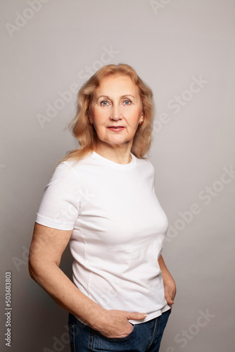 Happy mature old adult woman wearing white t-shirt standing against gray background