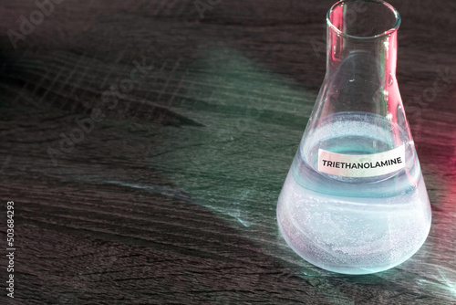 Chemical components: Triethanolamine. A clear chemical solution of triethanolamine in a flask. Flask with a substance on a wooden table. photo