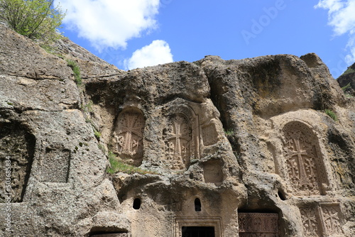 Ancient khachkars are built into the slope of the Geghard monastery complex, with shadows in the rays of the bright sun.