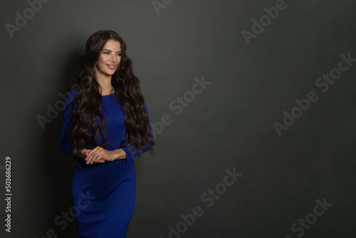 Beautiful young lady with long healthy hair and cute dress posing on dark gray background with copy space. Attractive brunette woman smiling © millaf