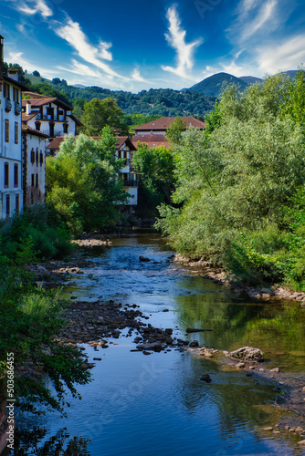 Half-timbered or baserri houses of Elizondo surrounded by trees and a river under a blue cloudy sky photo