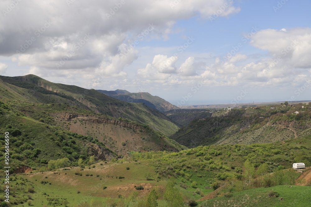 Green mountain valleys of Armenia under blue sky and clouds on a sunny day. Shadows from the clouds fall on the slopes and the valley and form bizarre shadows.