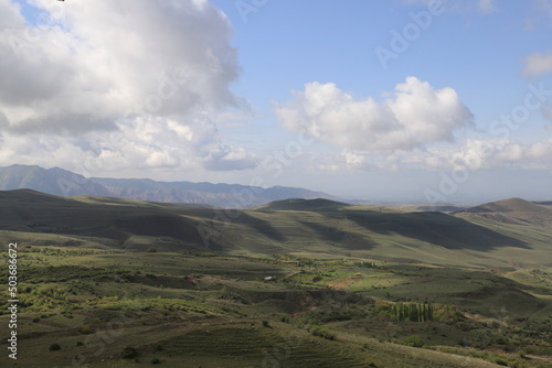 Green mountain valleys of Armenia under blue sky and clouds on a sunny day. Shadows from the clouds fall on the slopes and the valley and form bizarre shadows.