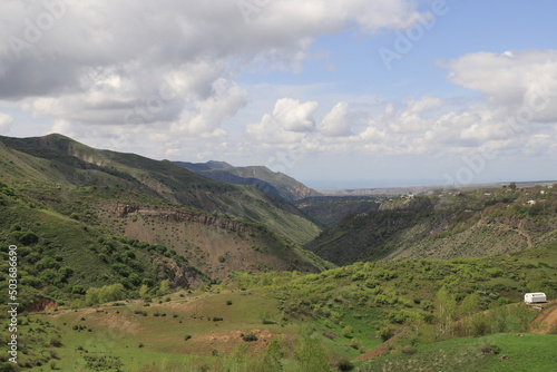 Green mountain valleys of Armenia under blue sky and clouds on a sunny day. Shadows from the clouds fall on the slopes and the valley and form bizarre shadows.