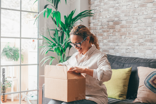Photos Overjoyed woman seated on sofa hold on lap small cardboard box open parcel clien