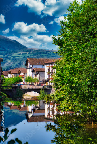 Half-timbered or baserri houses of Elizondo surrounded by trees and a river under a blue cloudy sky photo