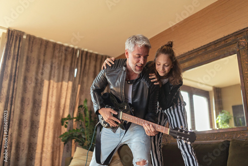 Fototapeta Naklejka Na Ścianę i Meble -  Father rock guitarist having fun and and dancing with his teenage daughter at home.