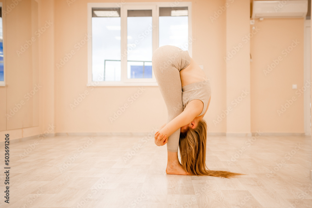 Fototapeta premium Young sporty woman, fitness instructor in sportswear doing stretching and pilates on yoga mat in the studio with mirror. Female fitness yoga routine concept. Healthy lifestyle and harmony.