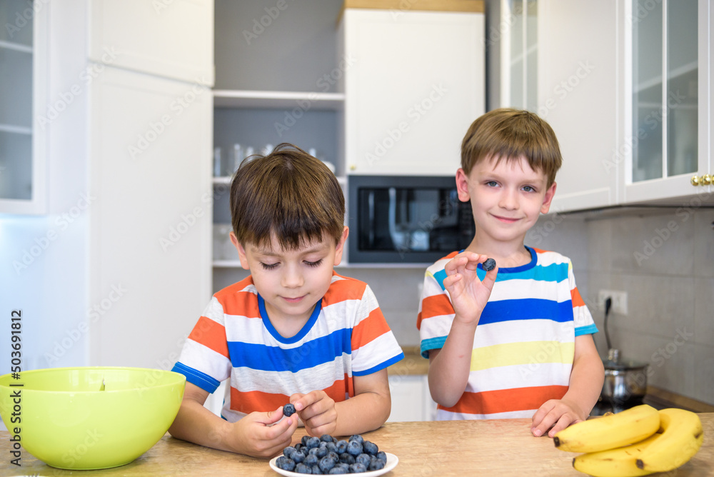 Happy child decorating meringue with blueberries . Child helping in kitchen