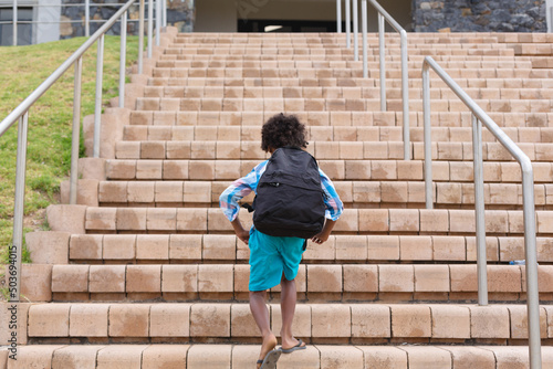 Rear view of african american elementary schoolboy with backpack climbing school building steps