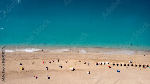 Aerial view of beautiful sandy beach with sunshades and soft turquoise ocean wave. Tropical sea in summer season on Kathisma beach on Lefkada island.