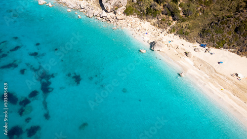 Aerial view of beautiful sandy beach with sunshades and soft turquoise ocean wave. Tropical sea in summer season on Megali Petra beach on Lefkada island.