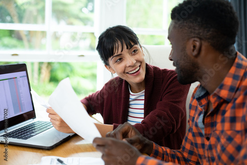 Happy multiracial young couple with laptop and bills discussing household expense budget at home