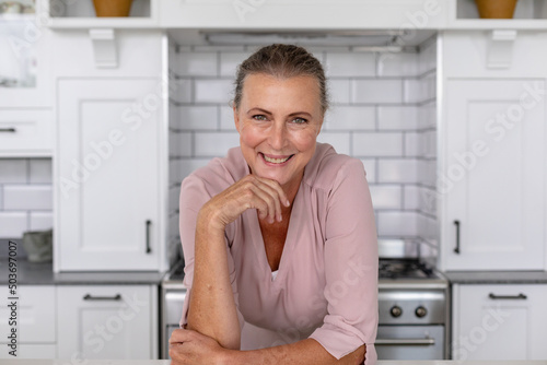Portrait of smiling senior caucasian woman leaning with hand on chin in kitchen at home