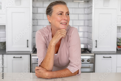 Smiling senior caucasian woman looking away leaning in kitchen at home