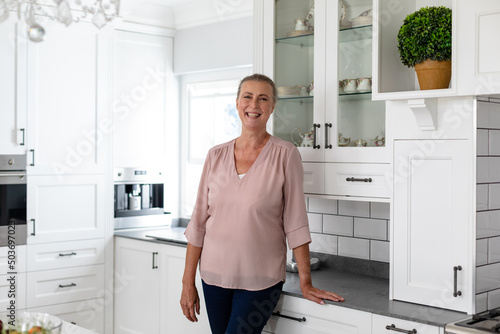 Portrait of happy senior caucasian woman standing by kitchen counter at home