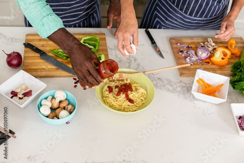 Midsection of senior multiracial couple preparing noodles at kitchen island