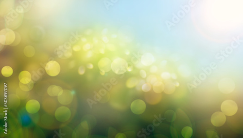A spring, summer background of fresh lush green foliage and blue sky with blurred bokeh highlights.