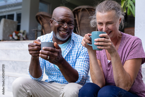 Happy multiracial senior couple having coffee together while sitting on steps