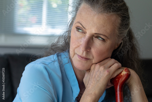 Thoughtful senior woman leaning on walking cane at home
