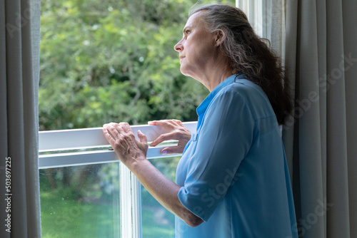 Contemplative caucasian senior woman looking away while standing at window in house