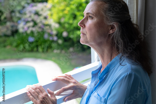 Contemplative caucasian senior woman looking away while standing at window