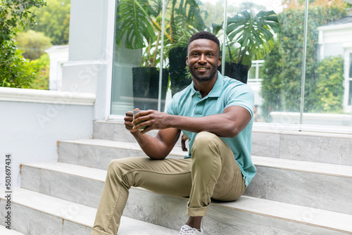 Portrait of smiling african american young man having coffee while sitting on steps outside house