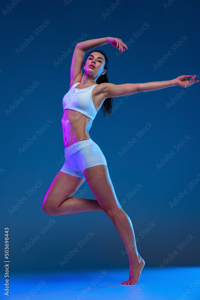 Portrait of young soprtive woman training isolated over blue studio background in neon light. Developing endurance