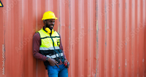 Portriat handsome male African American Industrial and factory Specialist. Black man worker wearing yellow protective hard hat helmet working at container yard.