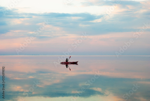 a boy swims along the estuary in a kayak during a beautiful sunset