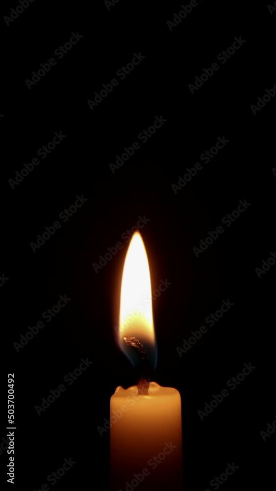 A single white candle is burning. Isolated burning candle on a dark background. A single white candle is burning. Isolated burning candle on a dark background.