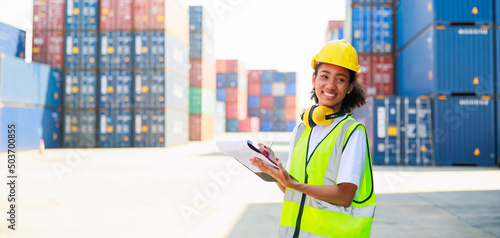 Black female dock worker control loading containers box from cargo at warehouse container yard. Marine and carrier insurance concept. logistic shipping yard