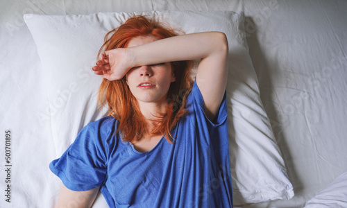 woman lying in bed with migraine and sensitivity to light covering her eyes photo