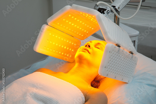 An elderly woman undergoes a facial rejuvenation procedure. Woman face lt Red light treatment At beauty clinic. Cosmetology.