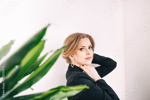 Portrait of a beautiful young woman on a white background, green houseplants nearby.