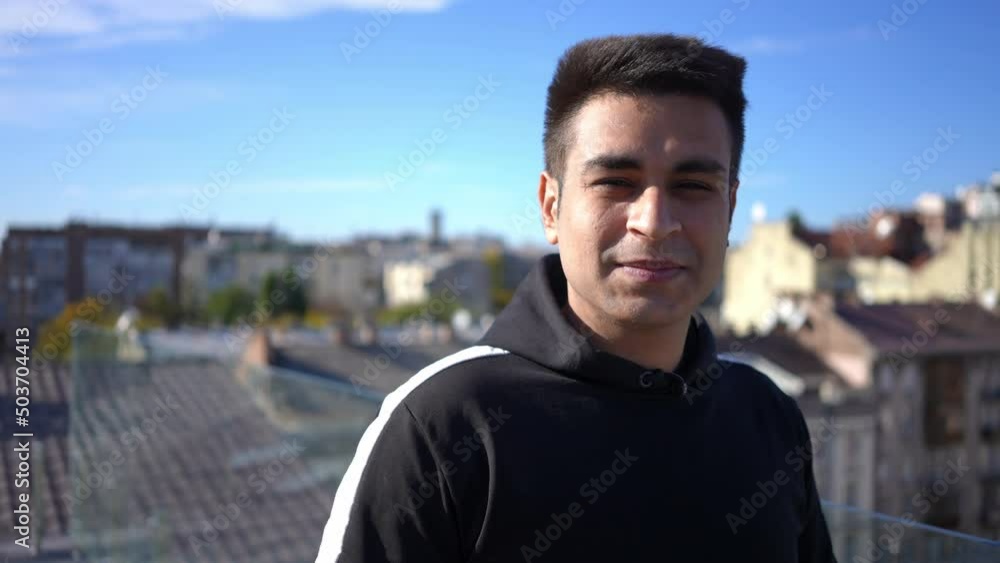 Portrait of positive Middle Eastern young man admiring sunny Kyiv Ukraine and looking at camera smiling. Happy male tourist enjoying leisure in sunshine on rooftop with urban city at background Portrait of positive Middle Eastern young man admiring sunny Kyiv Ukraine and looking at camera smiling. Happy male tourist enjoying leisure in sunshine on rooftop with urban city at background