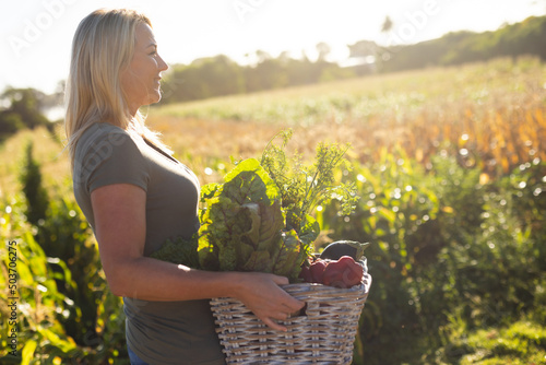 Side view of caucasian mid adult woman carrying vegetables while standing in farm during sunny day photo