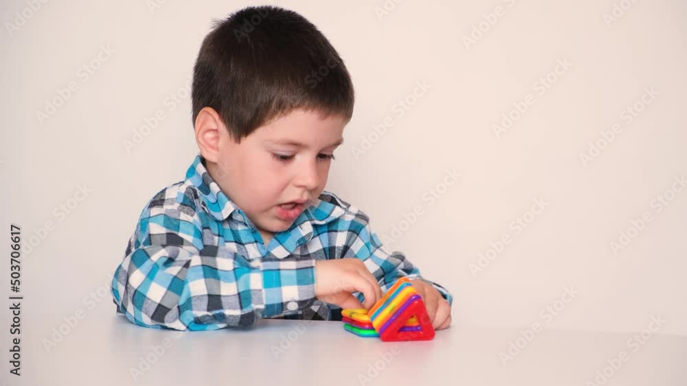 A preschool boy cheerfully plays with a magnetic constructor, laughs and speaks on a white background A preschool boy cheerfully plays with a magnetic constructor, laughs and speaks on a white background