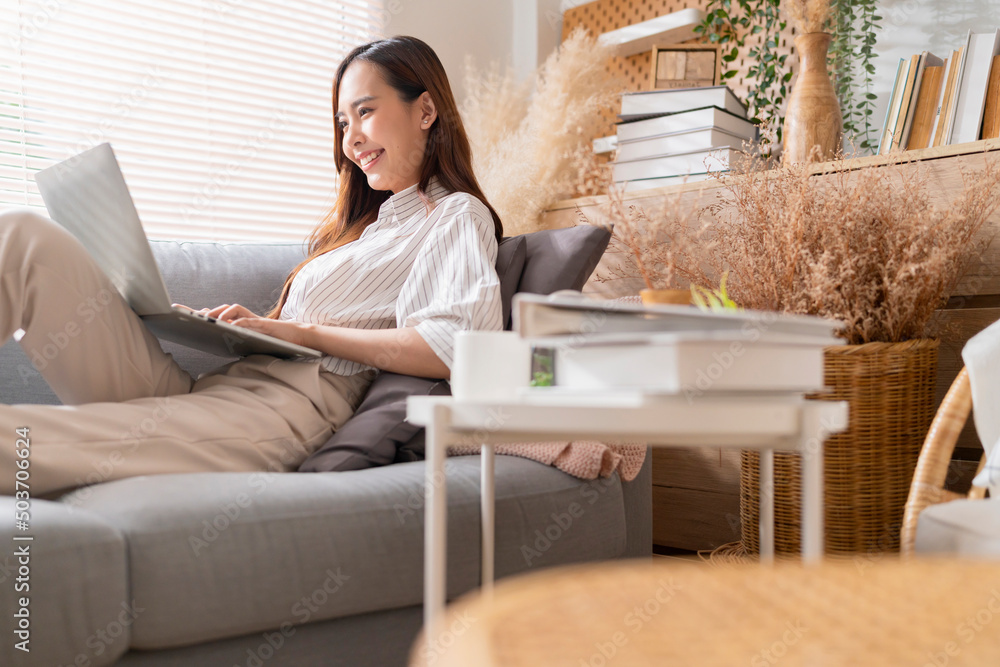 young attractive asian female working at home hand use laptop checking search schedule working process planning report with leisure relax on sofa in living room with morning light peaceful moment young attractive asian female working at home hand use laptop checking search schedule working process planning report with leisure relax on sofa in living room with morning light peaceful moment