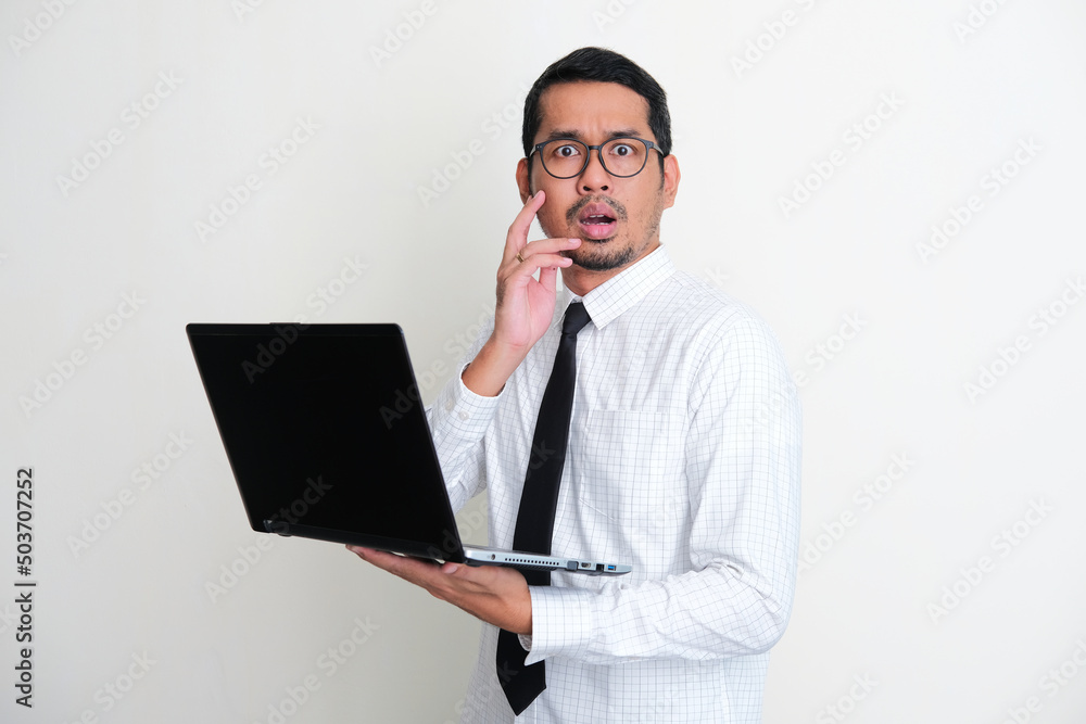 Asian businessman holding a laptop while showing shocked face expression Asian businessman holding a laptop while showing shocked face expression
