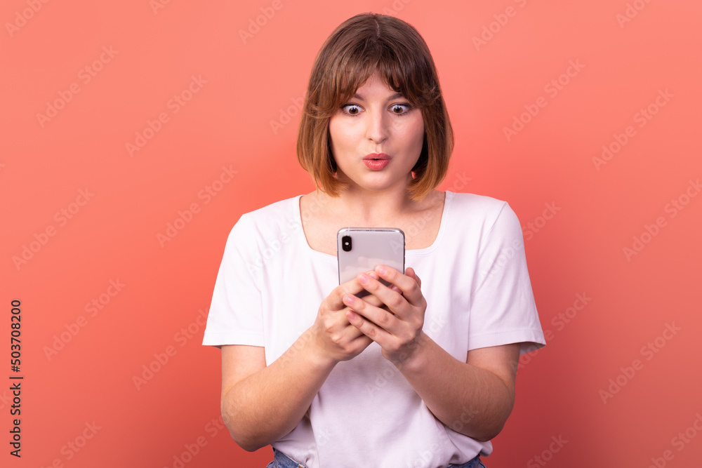 Portrait of a lovely amazed cheerful brown-haired woman using a 5g phone device as a reaction of delight and huge surprise, isolated on a pink pastel background. The concept of happiness and WOW Portrait of a lovely amazed cheerful brown-haired woman using a 5g phone device as a reaction of delight and huge surprise, isolated on a pink pastel background. The concept of happiness and WOW