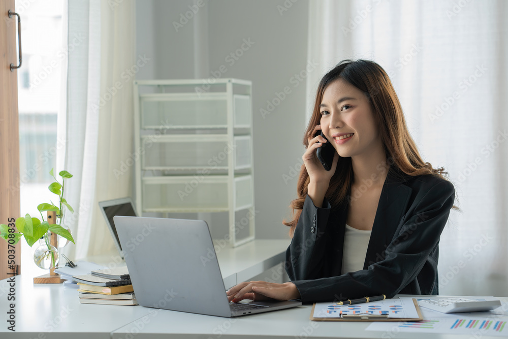Young Asian business women talking on mobile phone while working on laptop at desk office Young Asian business women talking on mobile phone while working on laptop at desk office