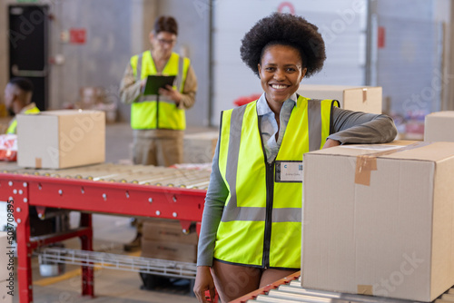 Portrait of smiling young woman standing by cardboard box and asian mature man working in background photo