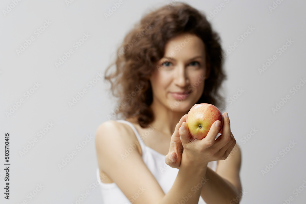 Smiling lovely cute curly beautiful woman in basic white t-shirt pulls apple enjoy healthy food posing isolated on over white background. Natural Eco-friendly products concept. Copy space Smiling lovely cute curly beautiful woman in basic white t-shirt pulls apple enjoy healthy food posing isolated on over white background. Natural Eco-friendly products concept. Copy space