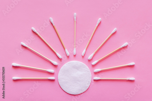 flat lay of ear sticks around white cotton pad on pink background  top view.