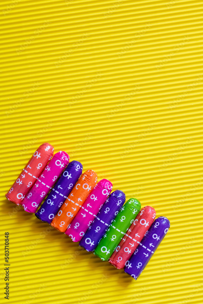 top view of packed multicolored tampons with female signs on yellow textured background. top view of packed multicolored tampons with female signs on yellow textured background.