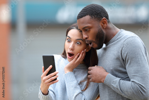 Foto Amazed interracial couple checking phone news