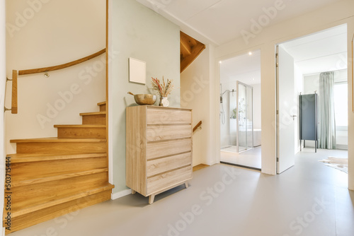 Hall of modern apartment with wooden stairs and commode