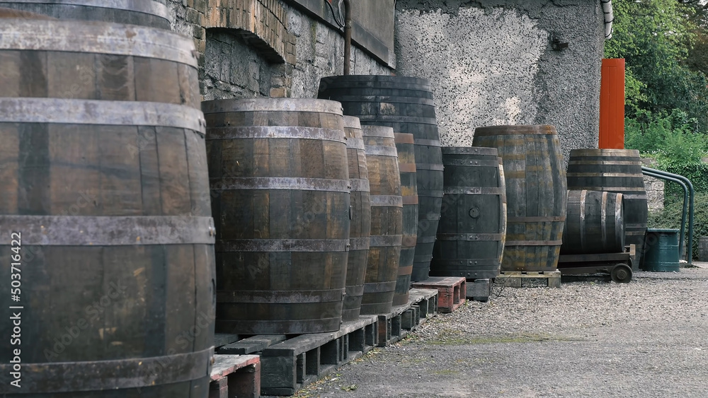 Wooden retro oak barrels are stored in rows in the backyard near the wall. Wine barrels
Wooden retro oak barrels are stored in rows in the backyard near the wall. Wine barrels