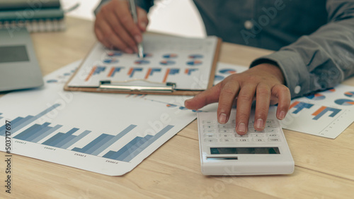 Young Asian businessman hand pressing a calculator to calculate, analyze, graph, finance, income and expenses, taxes, accounts, bills, credit cards, finance concept.